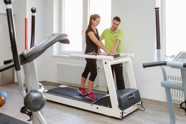 Ein Therapeut erklärt der Rehabilitandin auf dem Laufband Ein Therapeut erklärt der Rehabilitandin auf dem Laufband